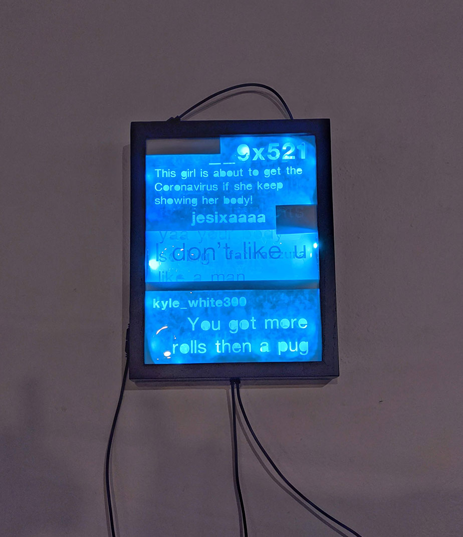 A light box from the Life Online exhibition: the box glows blue, and inside are multiple profane internet comments