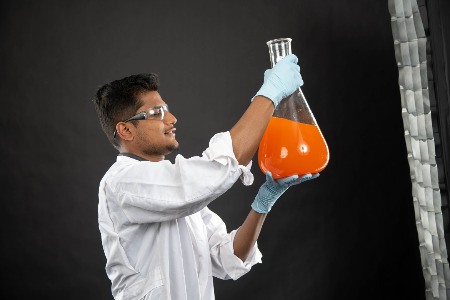 ISU student holding a beaker of orange liquid.