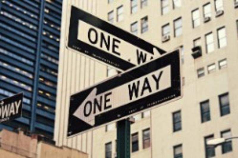 A street sign with arrows pointing the direction of a One Way street.