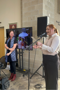 Stewart gives remarks at a microphone while Tara smiles nearby