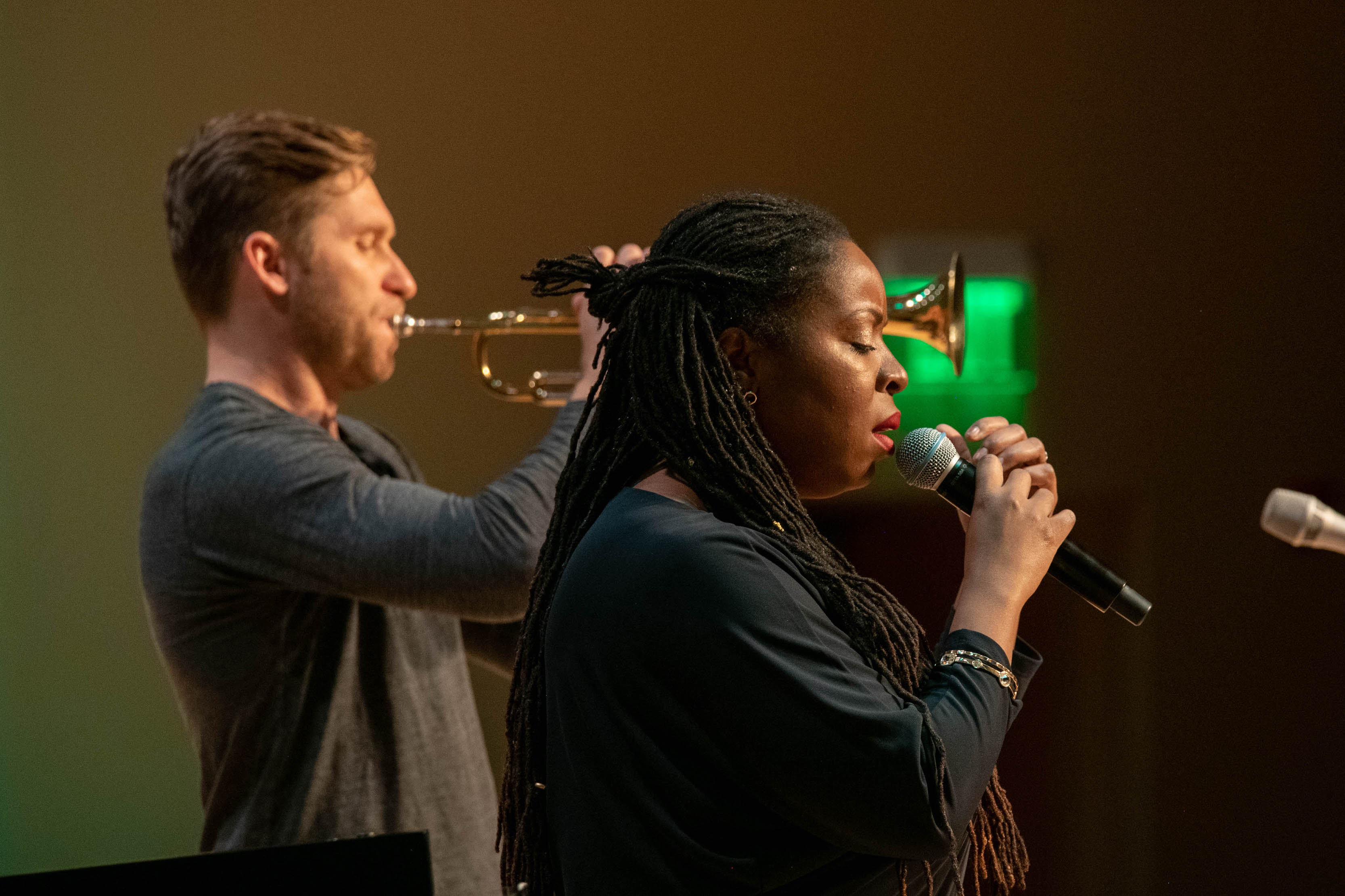 A person onstage playing trumpet and a person onstage singing in a microphone
