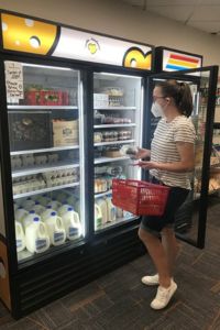 a student stands in front of a commercial freezer holding a shopping basket