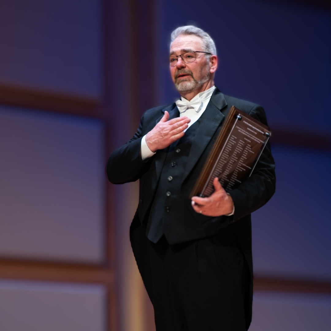 Scott stands onstage holding his plaque