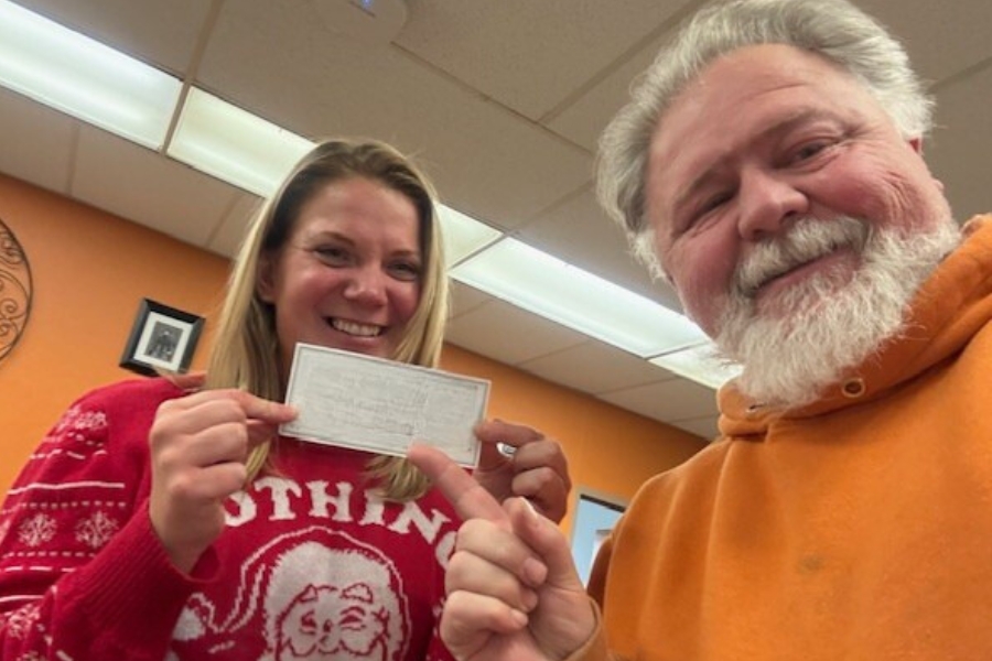 Tabitha and Brady stand together. Tabitha is holding a donation check and Brady, the donor, is pointing to it.