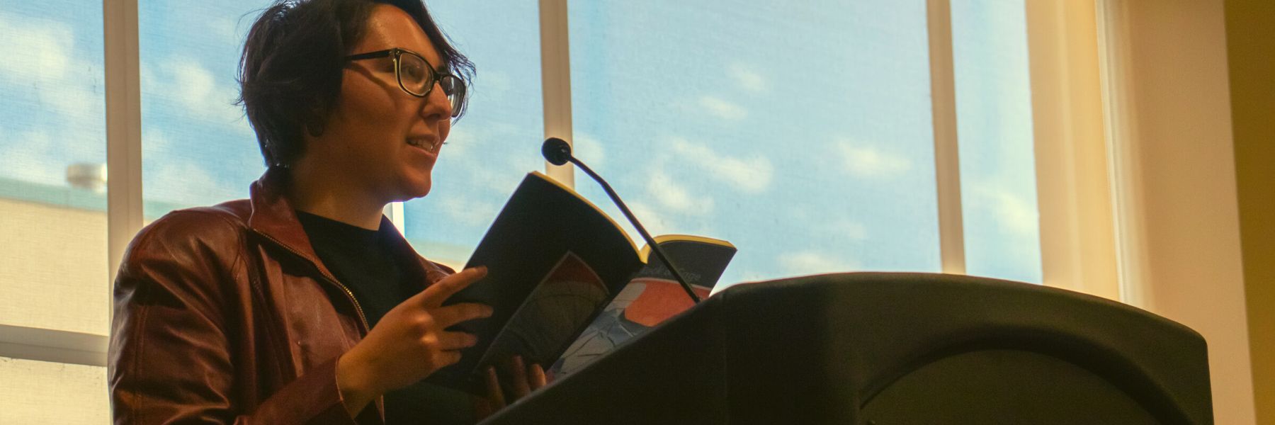 Student stands at podium holding a book and reading her published poem to the audience
