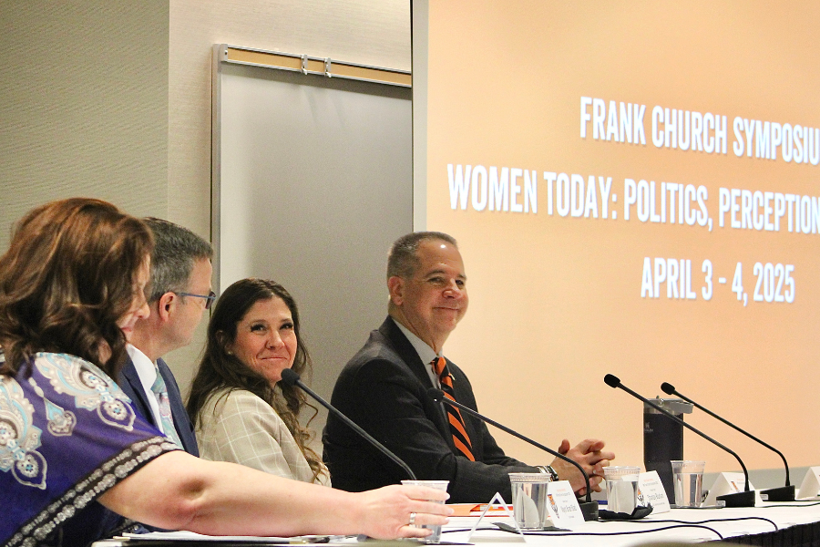 President Wagner and other panelists sit at a table with microphones and a presentation screen in the background