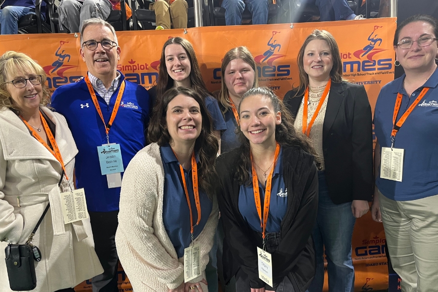 A group of eight people posing in front of an orange 