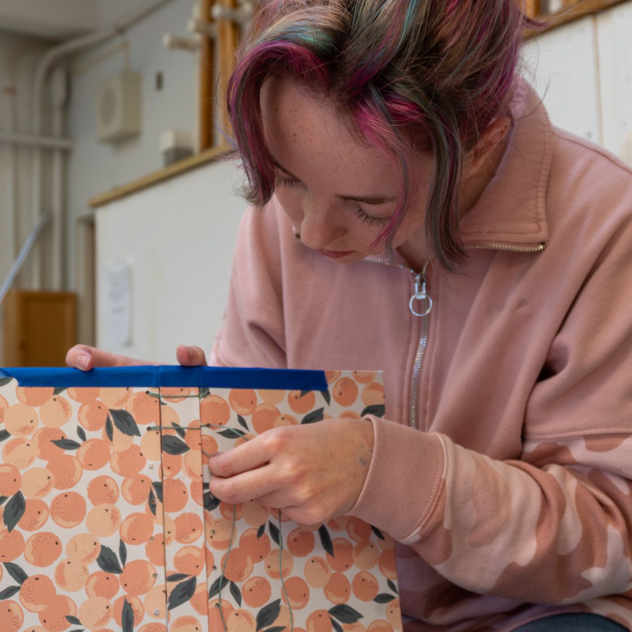 close up of a young woman piecing together a piece of fabric or paper that is pink with a floral print