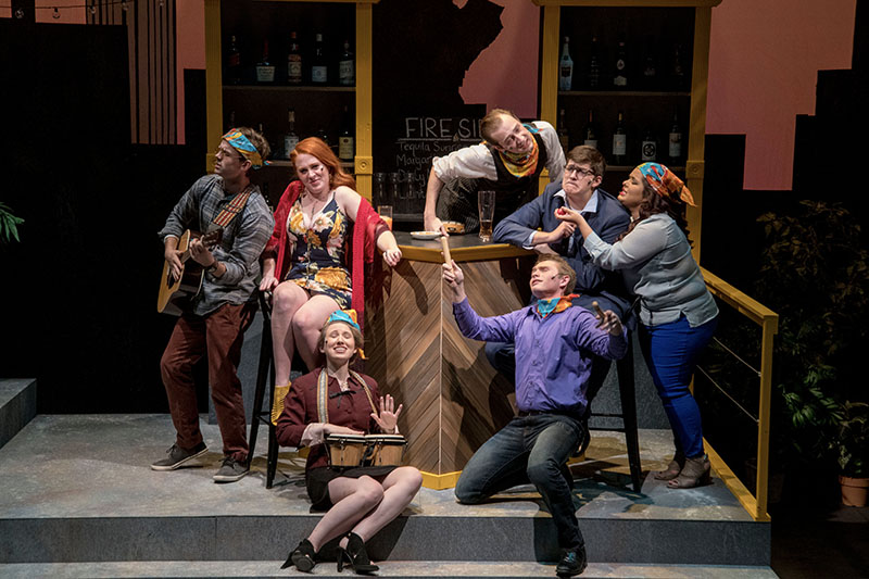 A cast in costumes performing onstage. Some are playing instruments.