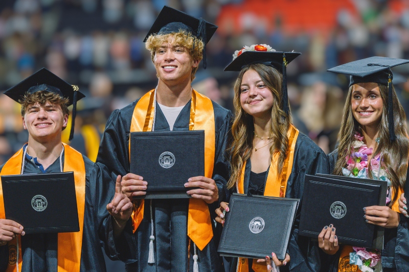 4 graduates at commencement holding their diplomas