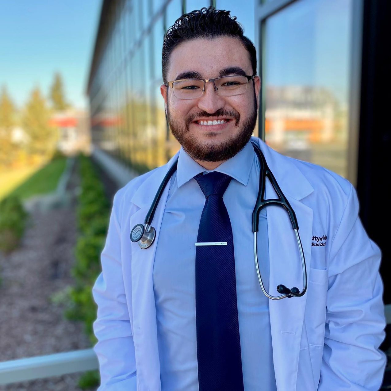 A student stands in a doctor's coat with a stethoscope around his neck