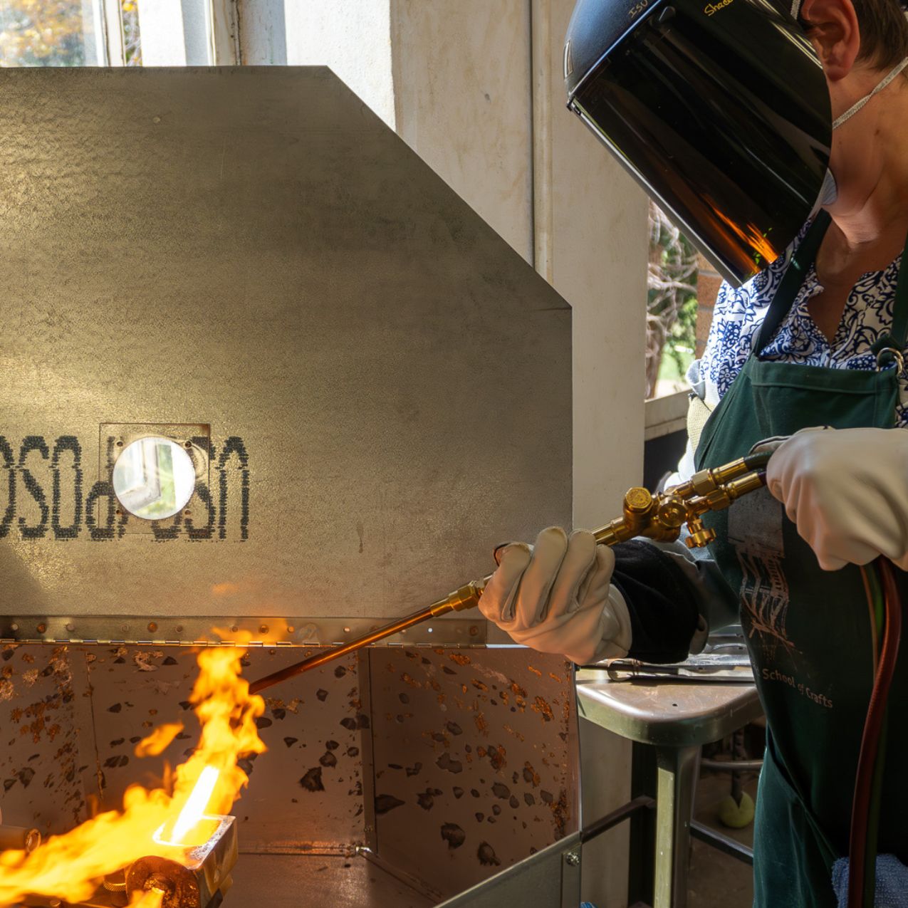 A person in welding protective gear works a blow torch near a kiln