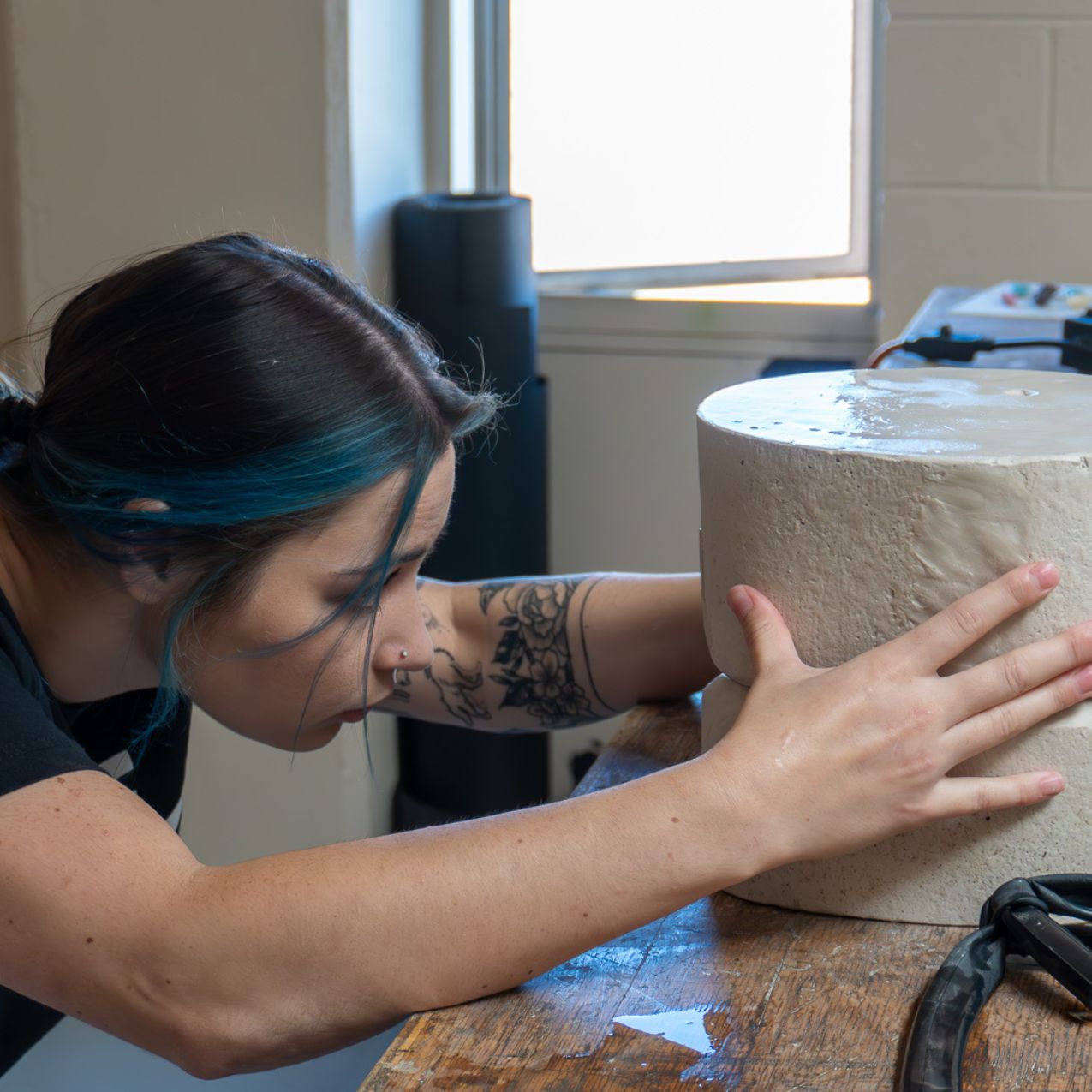 A young woman bends with her head close to a block of clay that she is working with her hands
