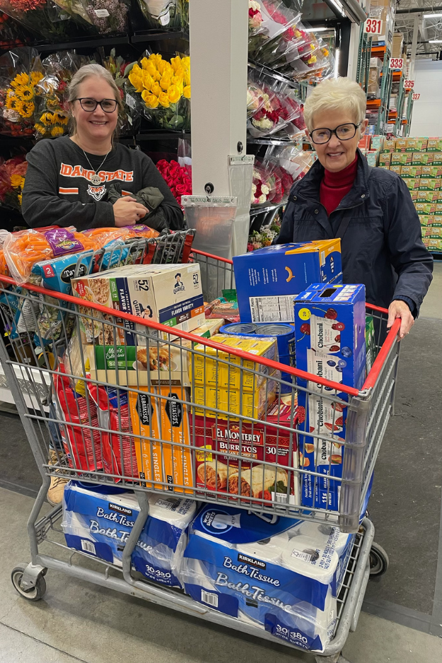 Lesa and Sharon stand behind a grocery cart full of food and toilet paper