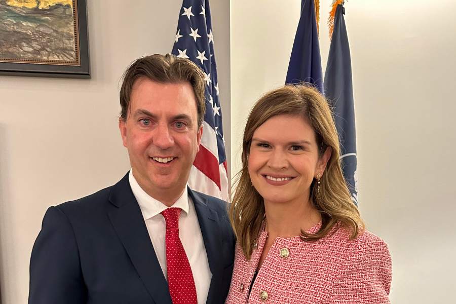 Mike and Luci Willits stand together in business attire in front of the American and Idaho flags