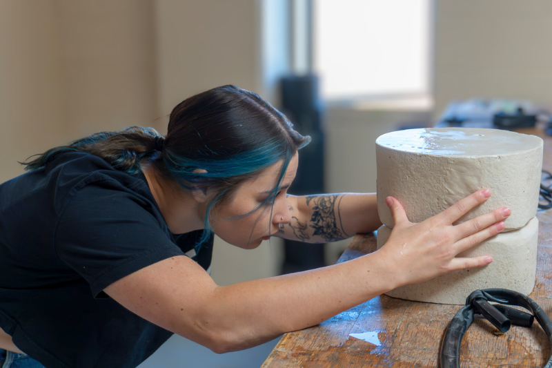 student bends toward a block of clay and works on it with hands