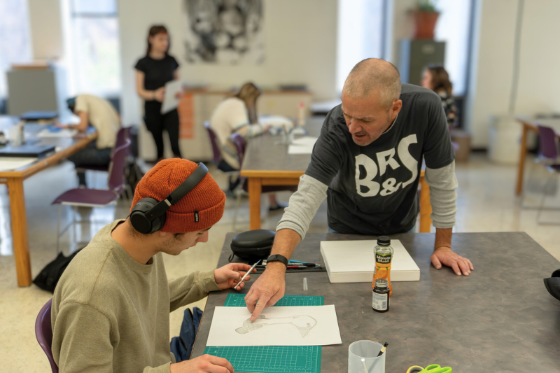 teacher gives instruction to student working on an art piece