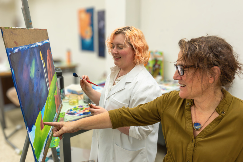 student paints on canvas while professor points out some feedback