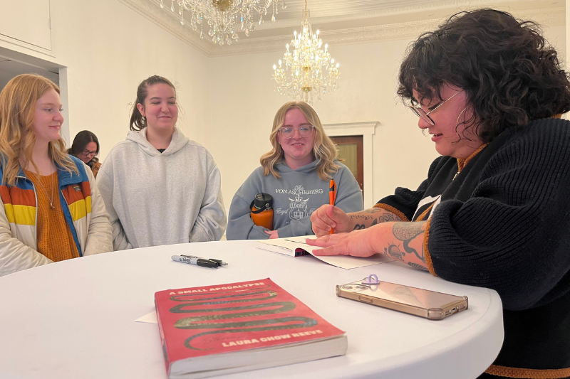 Three students watch while visiting author Laura Chow Reeve signs copies of their books