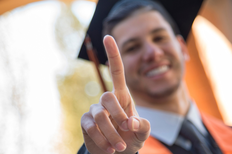 student in graduation regalia holds up a finger for 