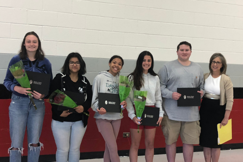 Five students holding their diplomas and flowers with Kandi Turley-Ames