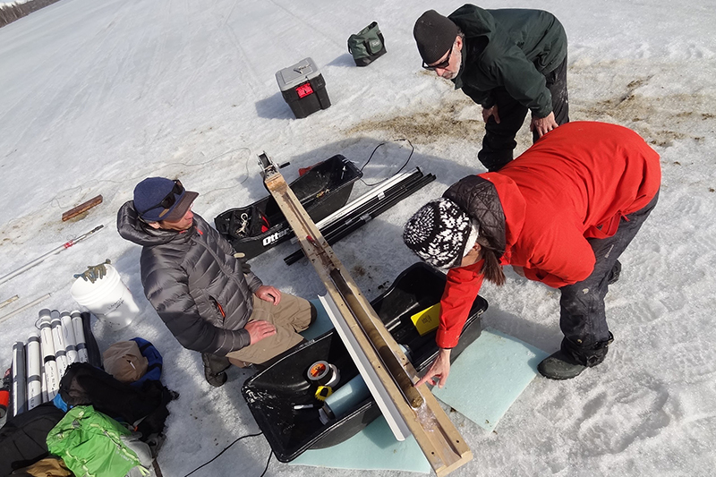 Brad Baxter, Lesleigh Anderson, and Bruce Finney examine a sediment core at April Fools Lake. Photo credit: Carson Baughman and Lesleigh Anderson, courtesy of the U.S. Geological Survey