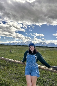 Emma Pearson in front of a log fence with clouds in the bacground