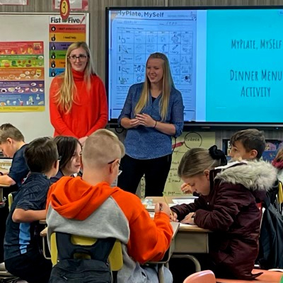 Two dietetics students standing the front of an elementary classroom giving a presentation