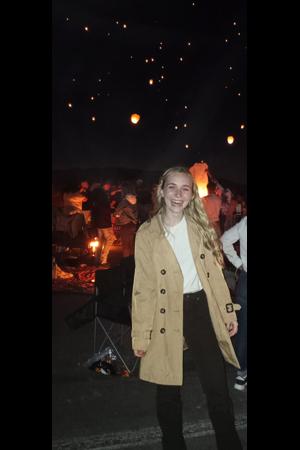 Aspen Brown, smiling at an outdoor event with a crowd in the background and glowing sky lanterns.