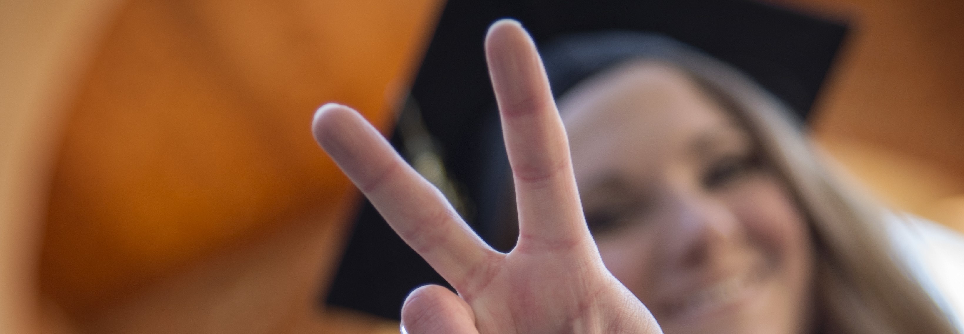 Student wearing cap and gown holding up a peace sign