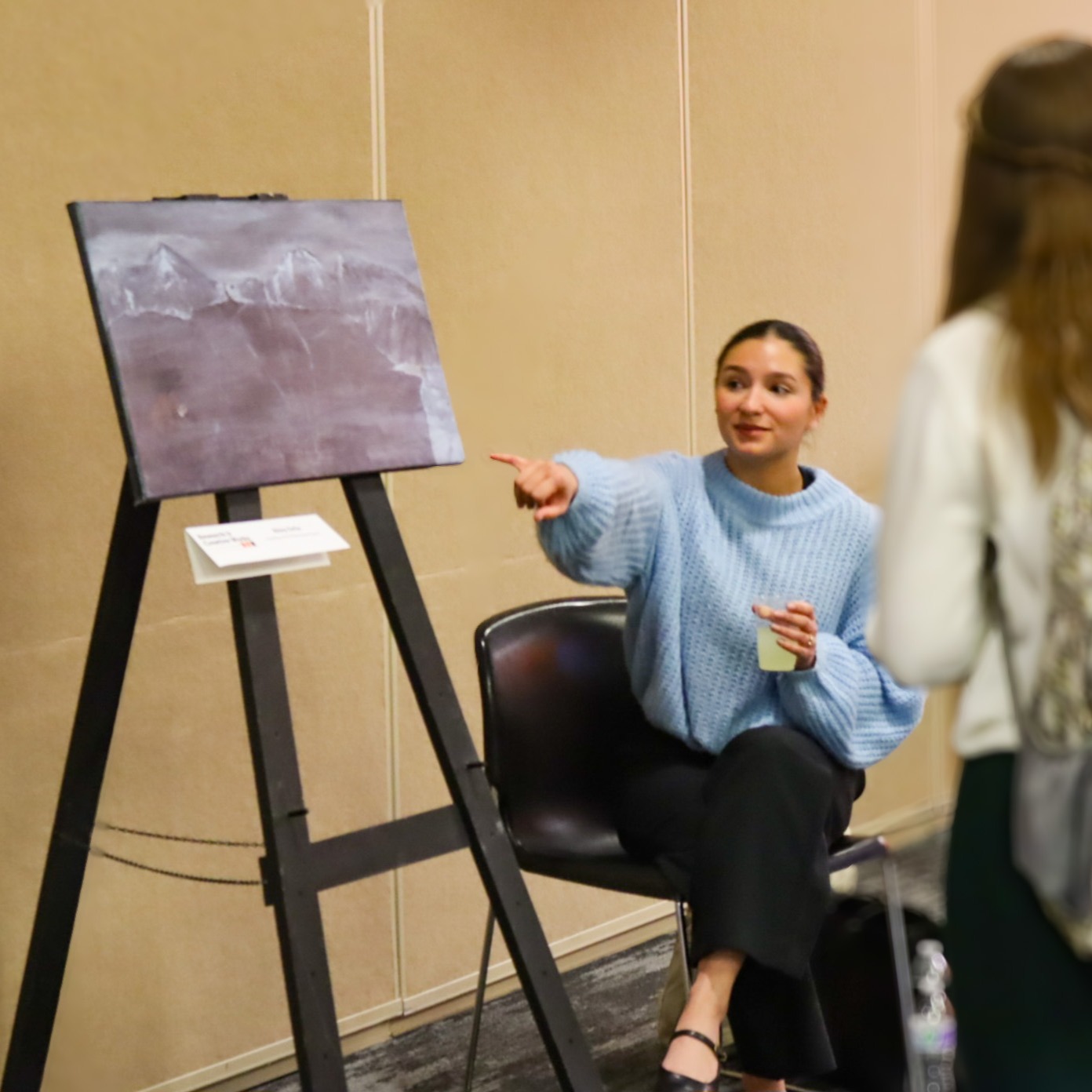 A student points at and presents her painting to another student