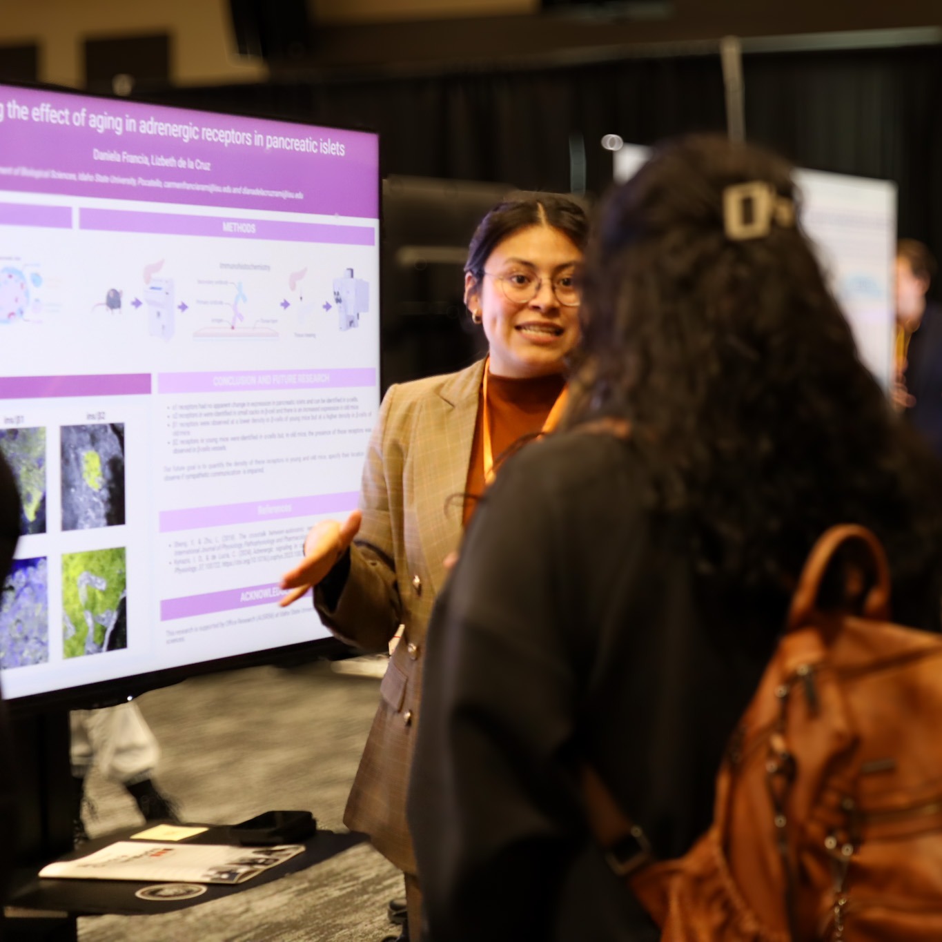 a student presenting her poster on a tv to a few people