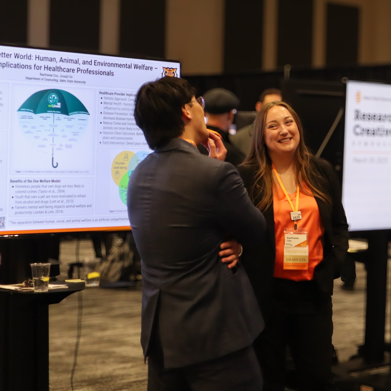 2 students standing in front of a tv poster