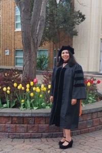 Najmeh Dehghanitafti posing in her graduation robes in front of a bed of flowers