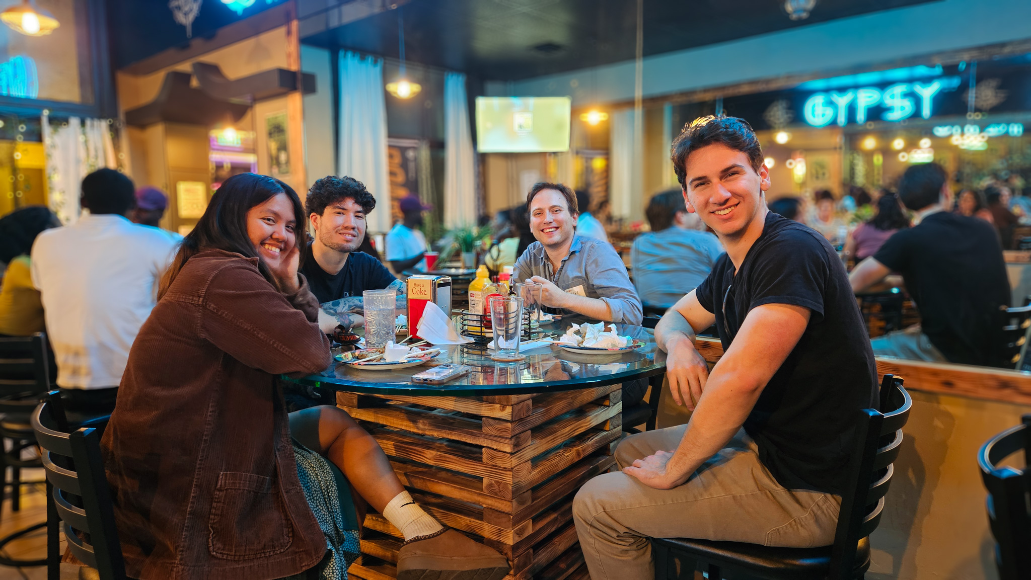 A group of 4 students at Late Nights sitting at a table and smiling at the camera