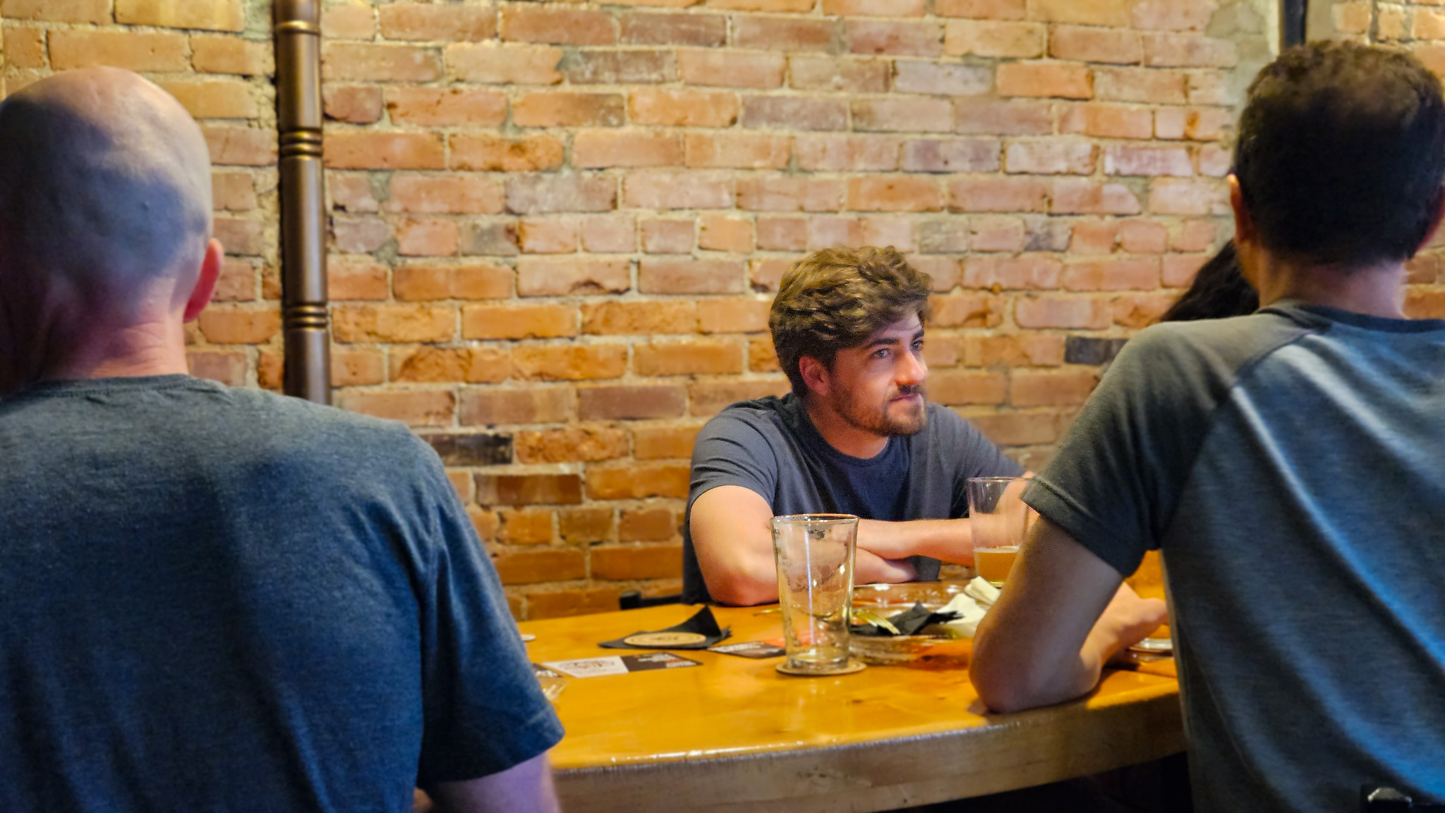 Man sitting at a table at late Nights with a drink talking to someone across from him