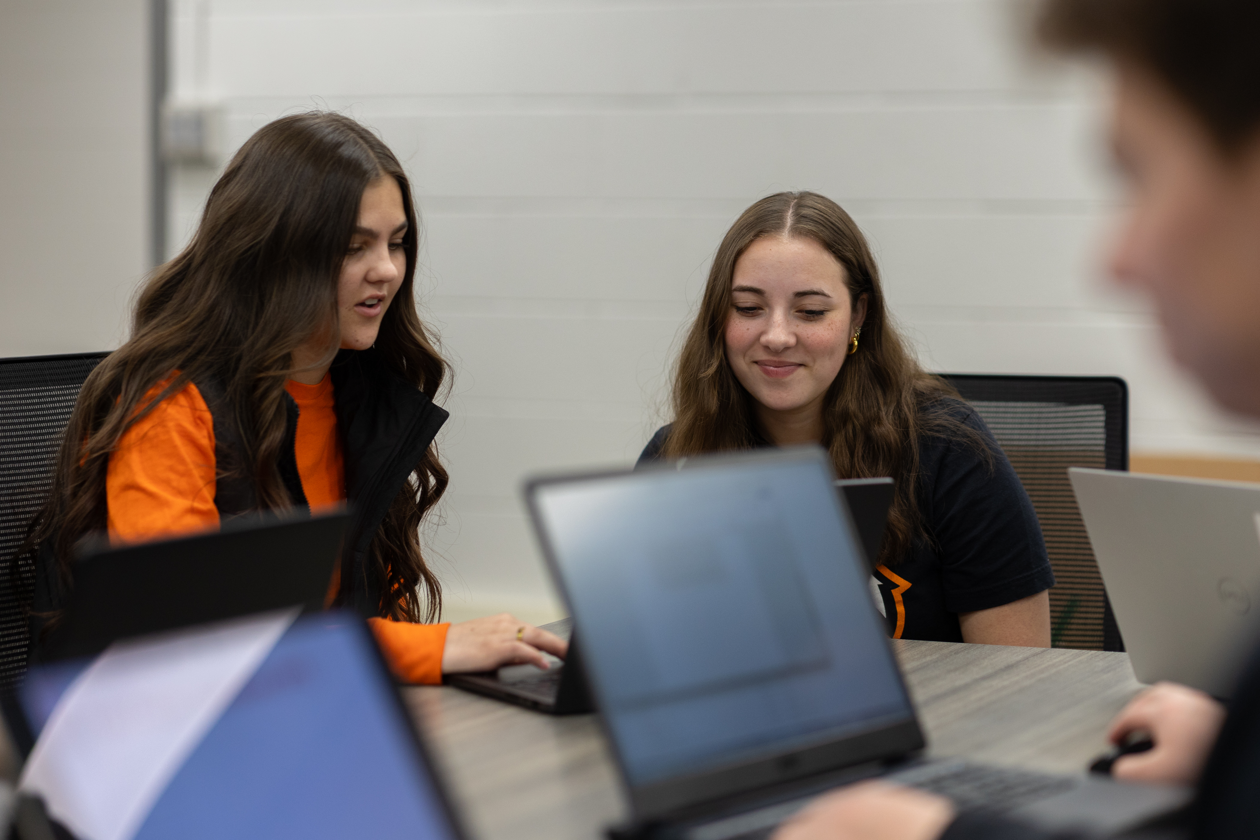 Two students sitting at a table and viewing something on a laptop