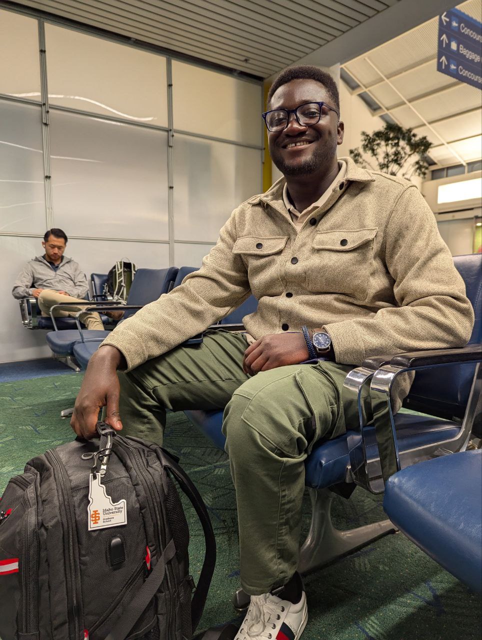 Man sits in airport holding backpack with an ISU Graduate School luggage tag on it