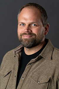 A headshot of a middle aged man with dark hair and facial hair