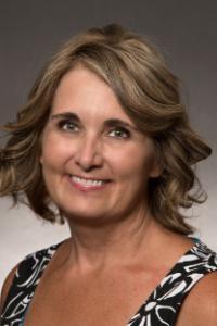 A woman with medium skin tone, blond hair, she is wearing a black and white blouse