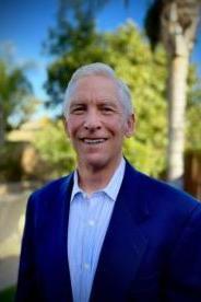 A man with white hair, medium skin tone, wearing a blue shirt and a dark blue suit jacket