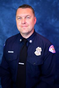 A man with light skin tone and brown hair. He is wearing a police uniform
