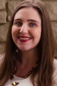 A woman with light skin tone and long brown hair, wearing a white shirt