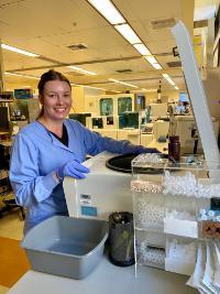 A woman wearing scrubs and gloves standing over a centrifuge