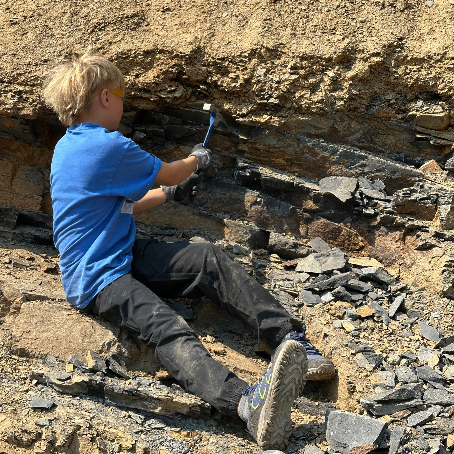 Middle school aged male using a pick axe to find trilobites on a slope