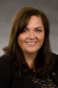 A medium skin toned woman with brown hair. She is wearing a black shirt and smiling.