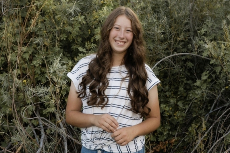 smiling female with long brown hair standing in front of dense green vegetation