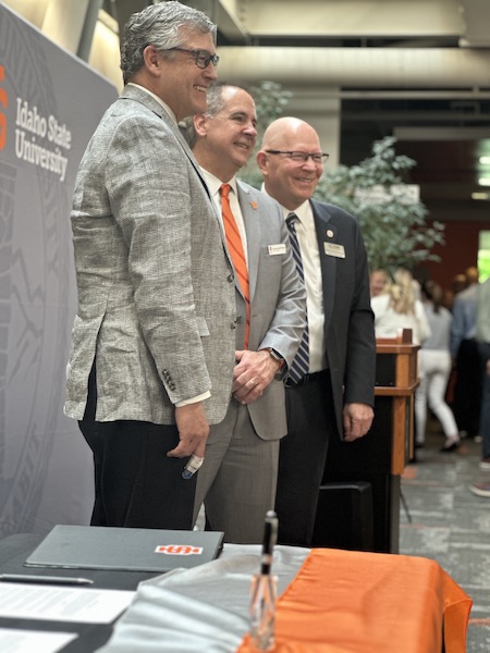 Three men stand at a table