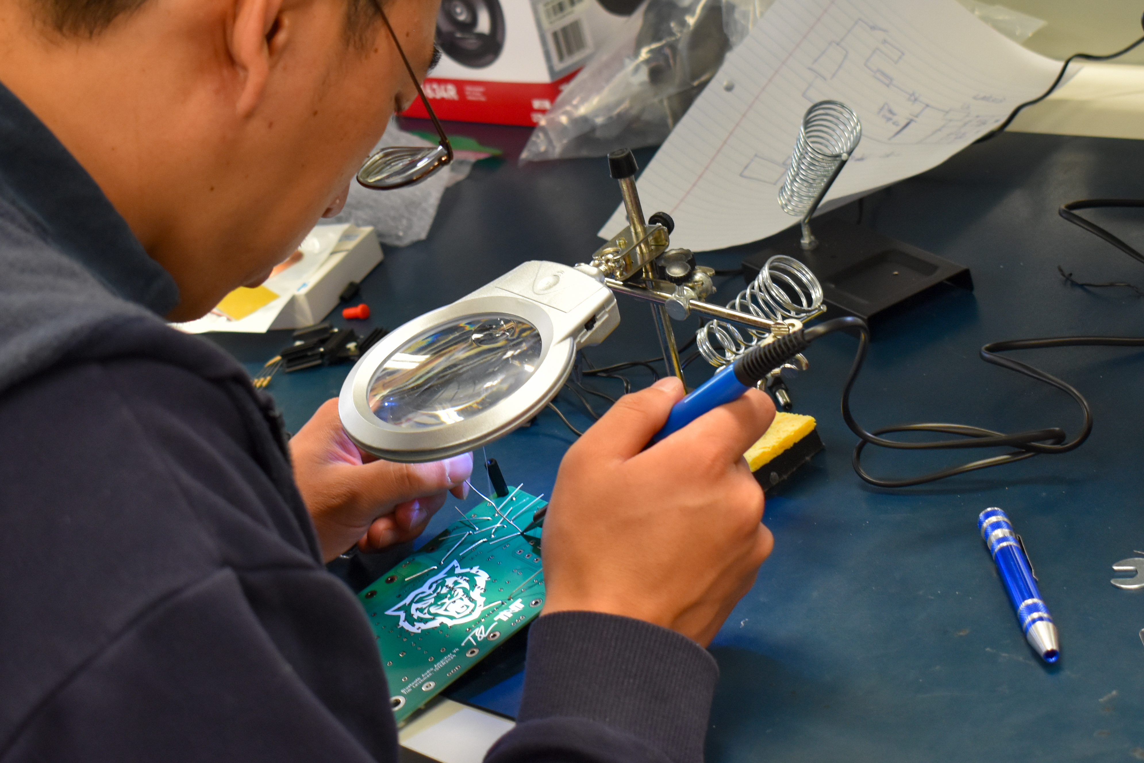 Man using a magnifying glass to work on a soldering project