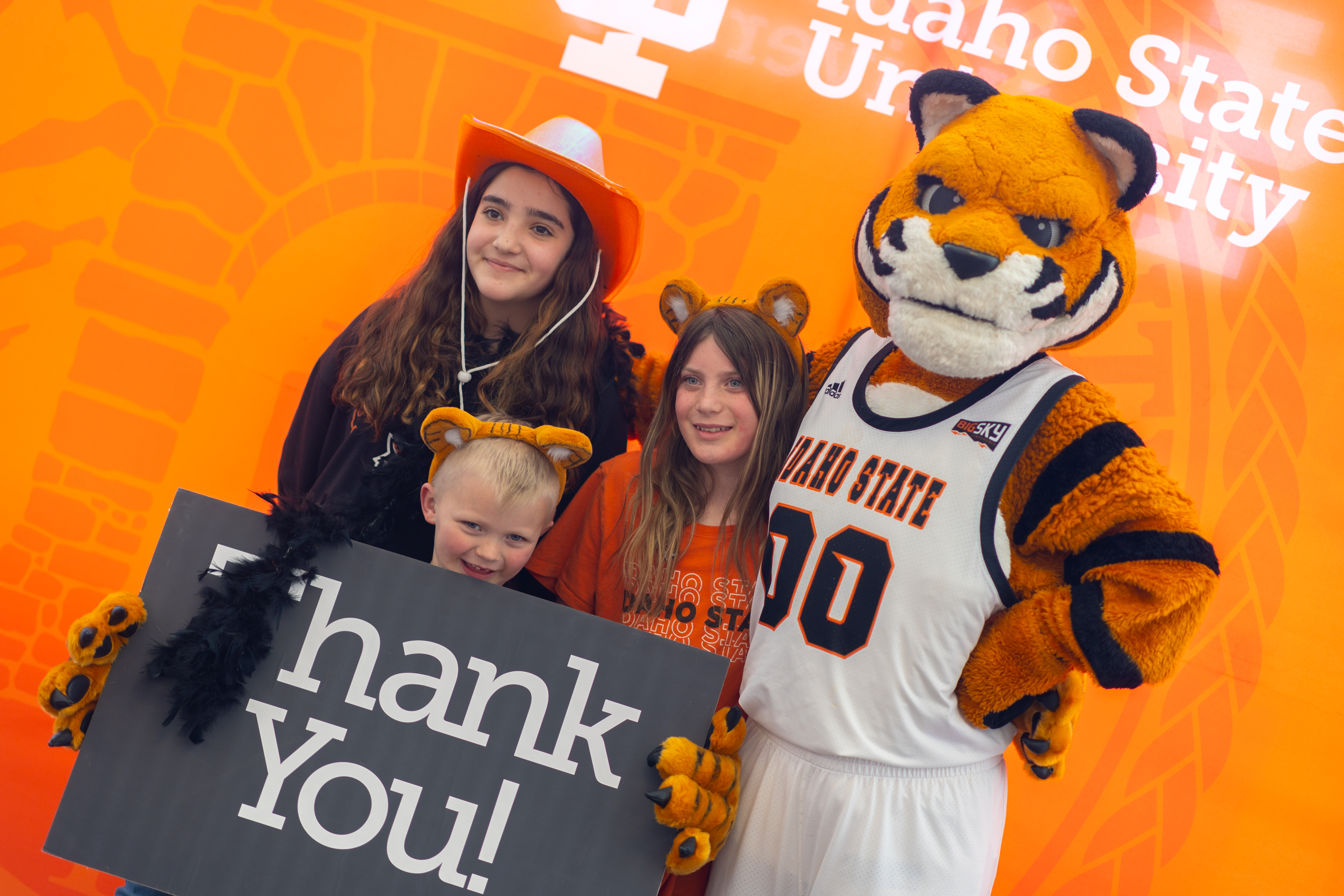 Benny Bengal and three children celebrate Bengal Giving Day success with a sign saying Thank You
